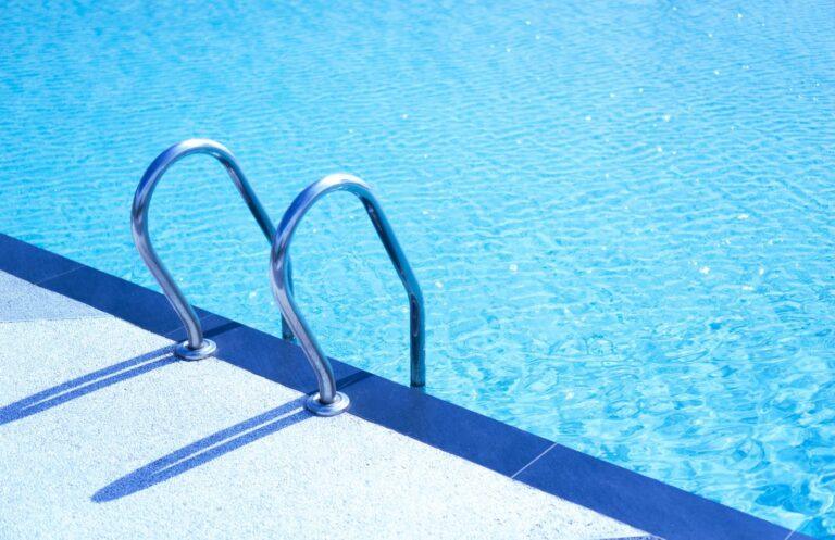 Geef een verouderd zwembad een complete tweede levensfase Metal ladder leading into a refreshing turquoise swimming pool, perfect for a summer vacation.