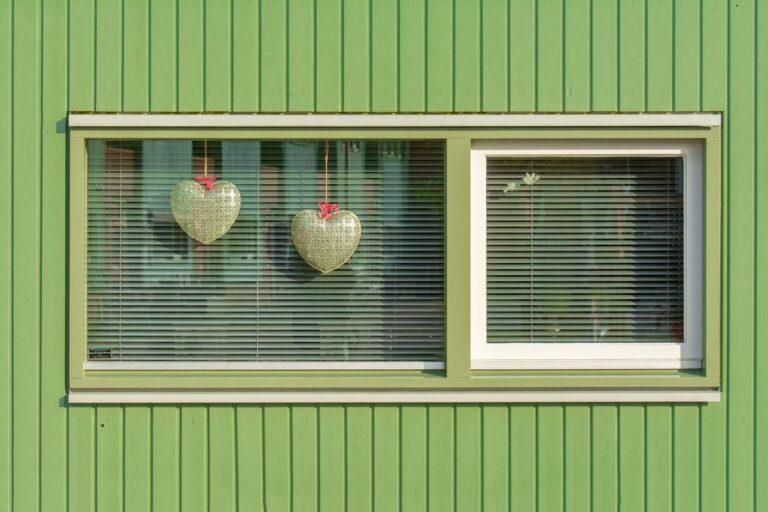 Green house exterior with two heart decorations in a window.