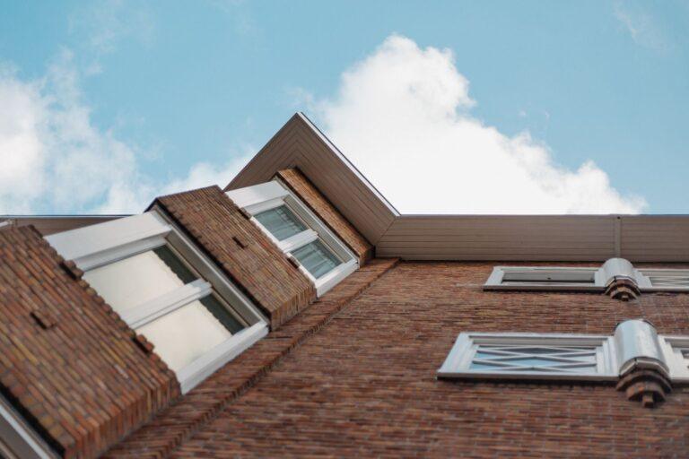 Invloed van gevelonderhoud op de waarde en uitstraling van uw huis Low angle shot of a brick building with glass windows against a clear blue sky.
